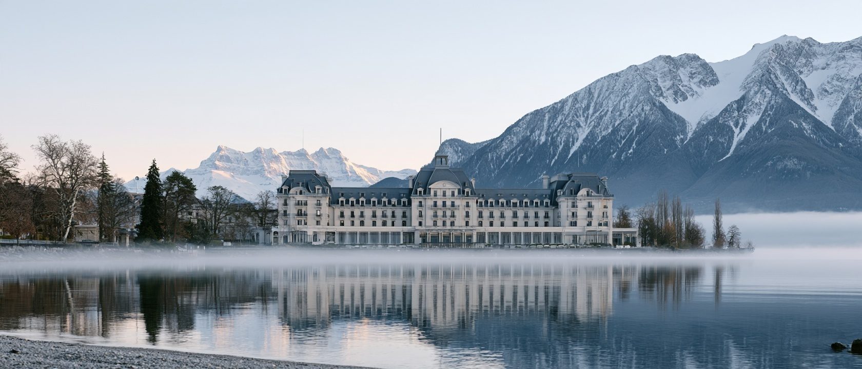 A grand lakeside hotel on Lake Geneva at dawn with the Alps beyond